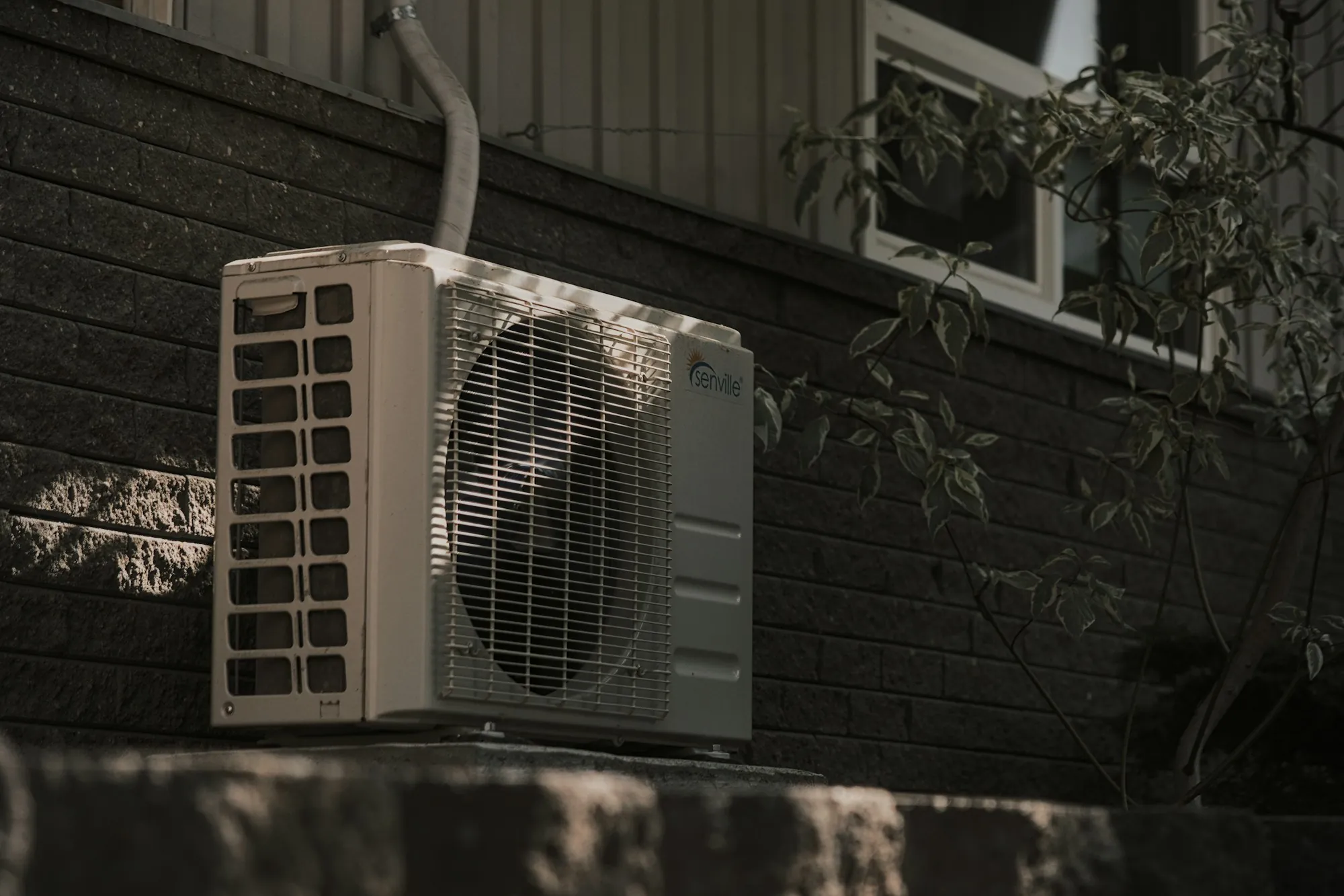 Mini-split outdoor condenser mounted on a dark brick wall