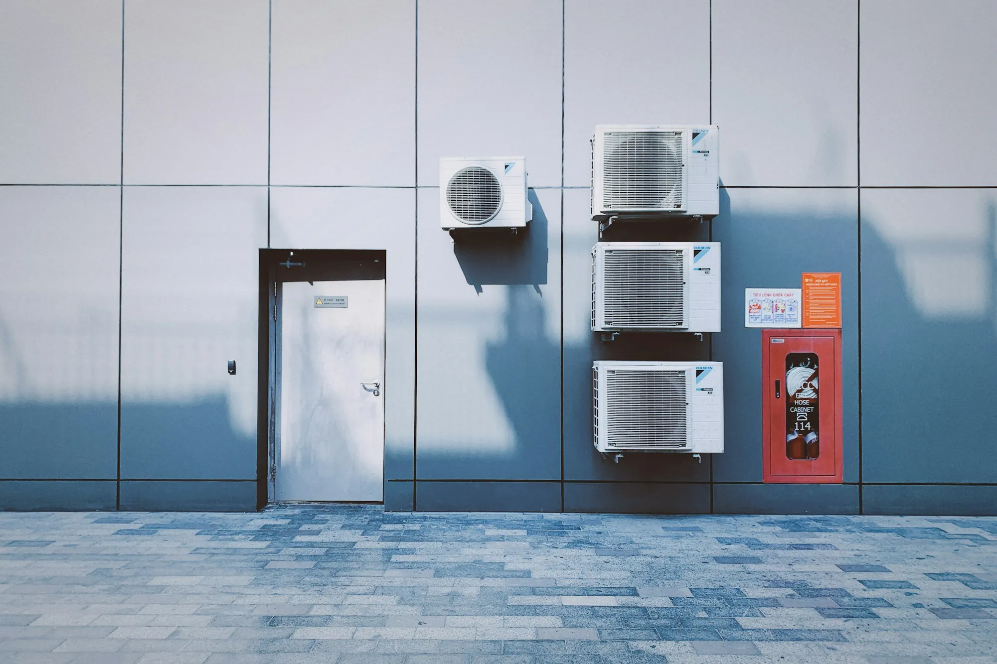 Stacked mini-split condensers on a gray building wall
